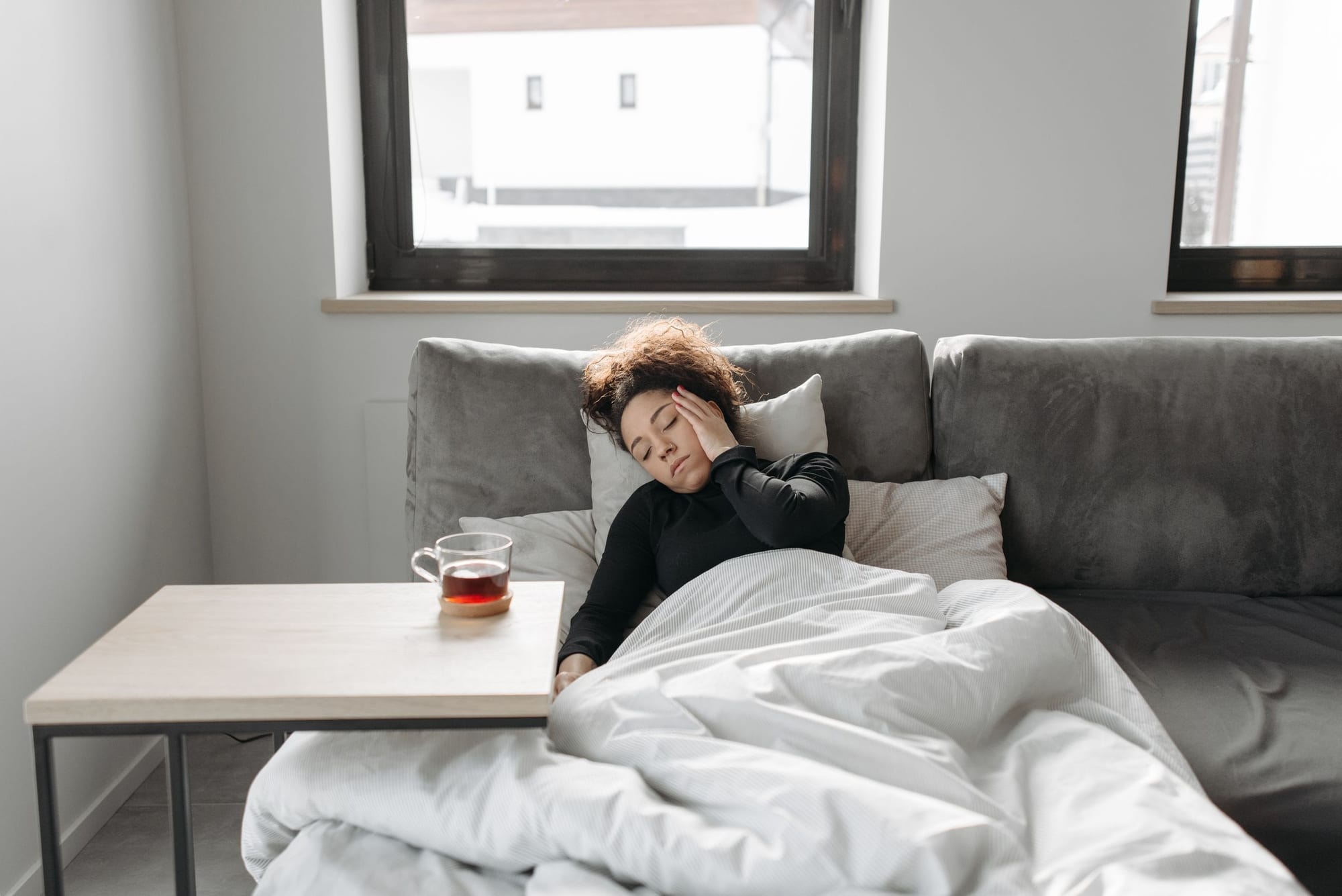 Förkyld person med te och filt i soffan