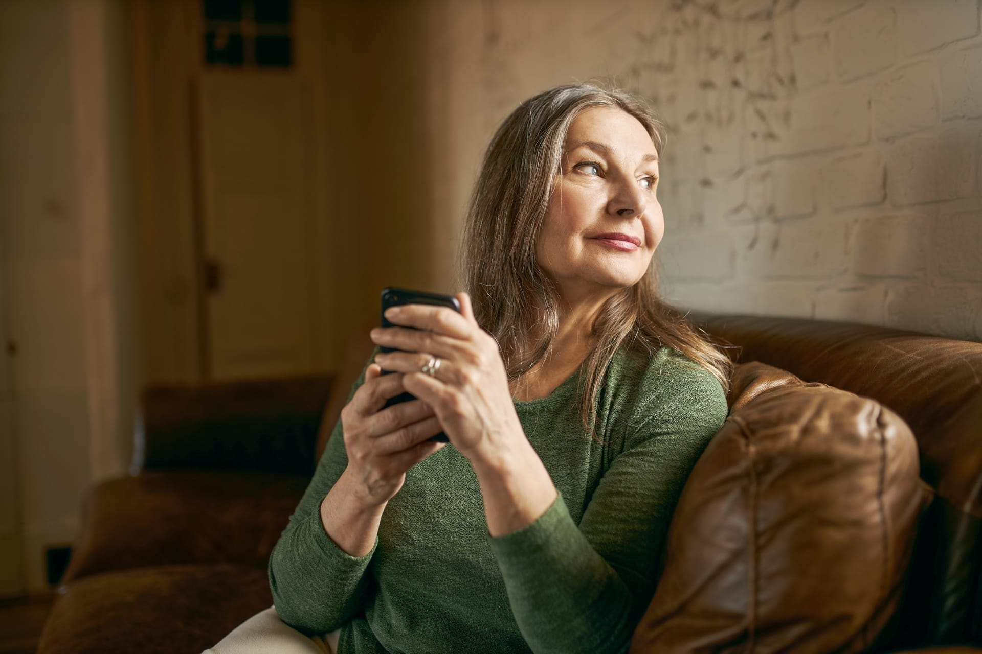 Kvinna i soffa som tittar ut genom fönstret med mobilen i handen