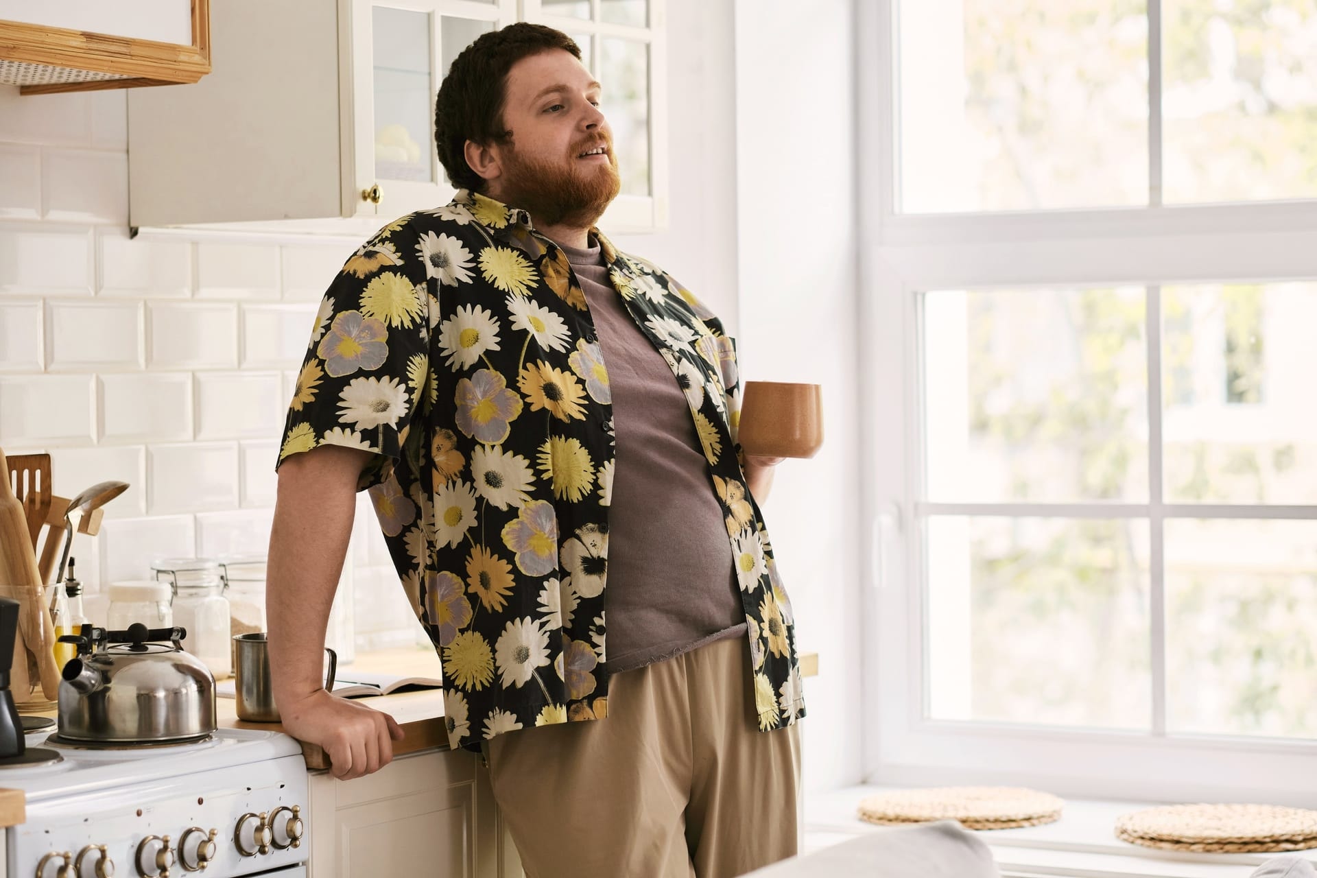 Man i blommig skjorta som dricker kaffe i sitt kök