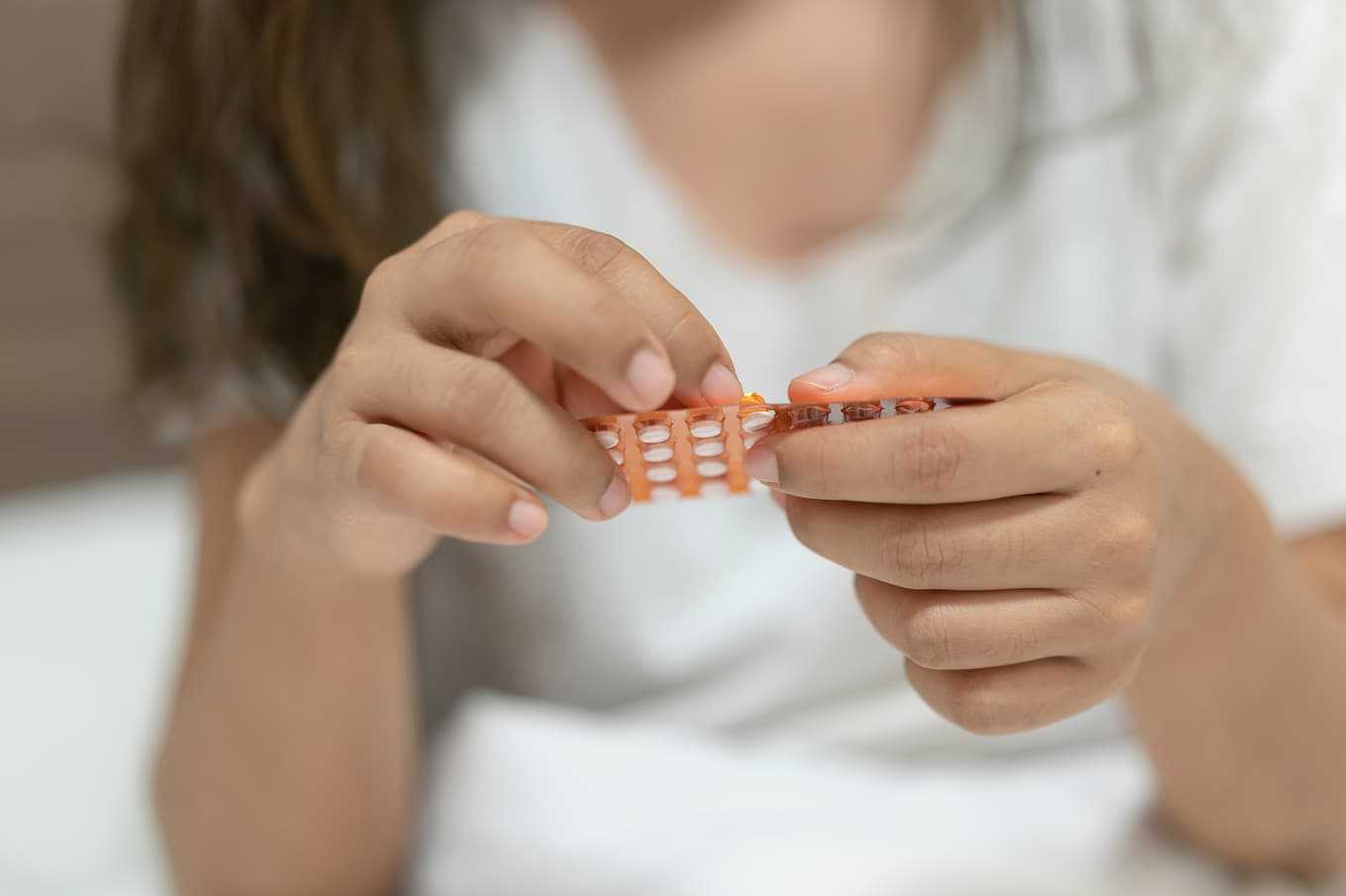 Närbild av en kvinna som tar ett piller för att skjuta upp mensen. Hormonella läkemedel kan användas för att senarelägga menstruationen vid behov. Läs mer om metoder, fördelar och biverkningar av att skjuta upp mensen på Doktera.
