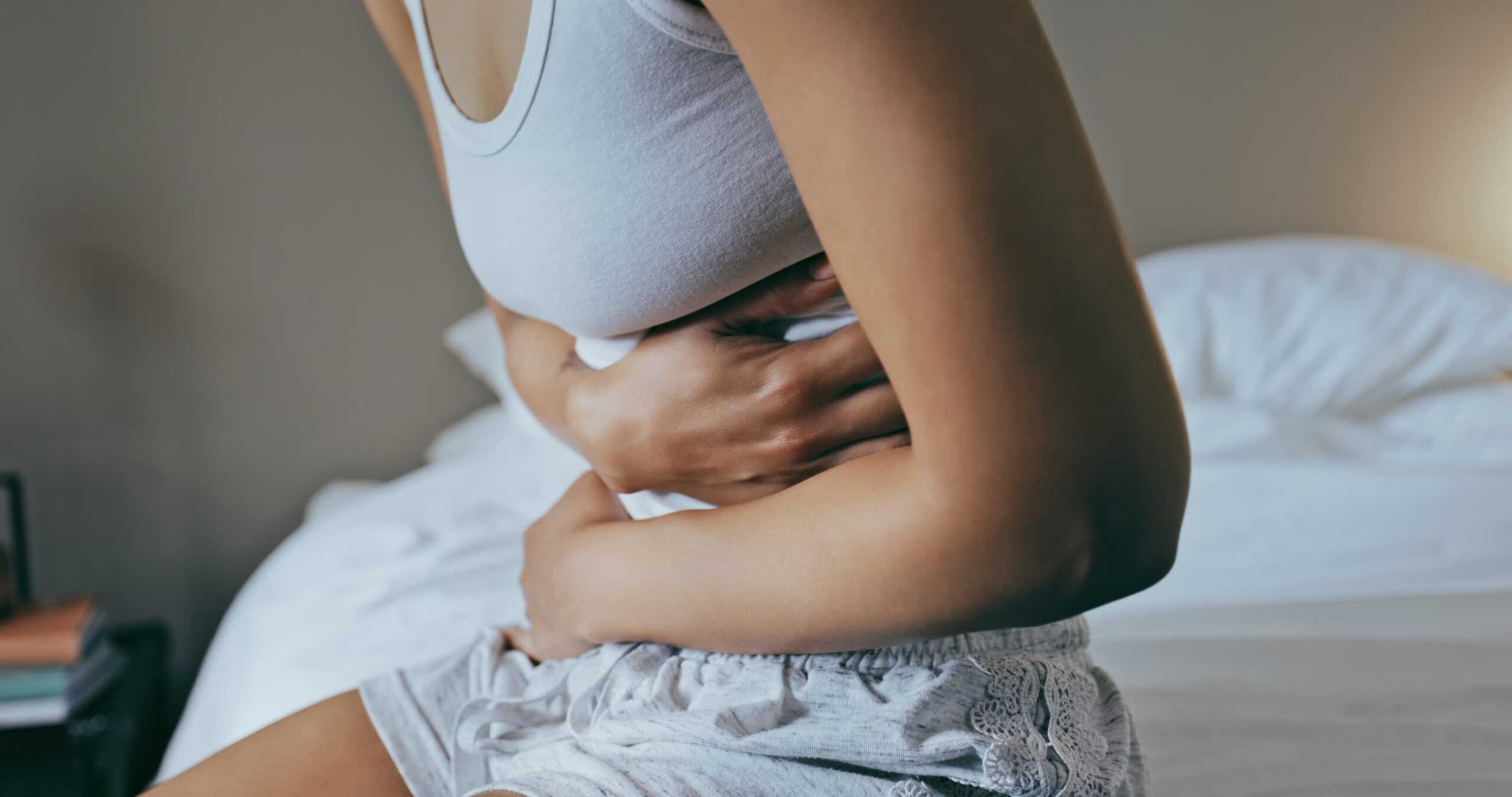 Kvinna med mensvärk håller sig om magen i sängen – typisk smärta vid menstruation med kramper och obehag i nedre delen av magen.