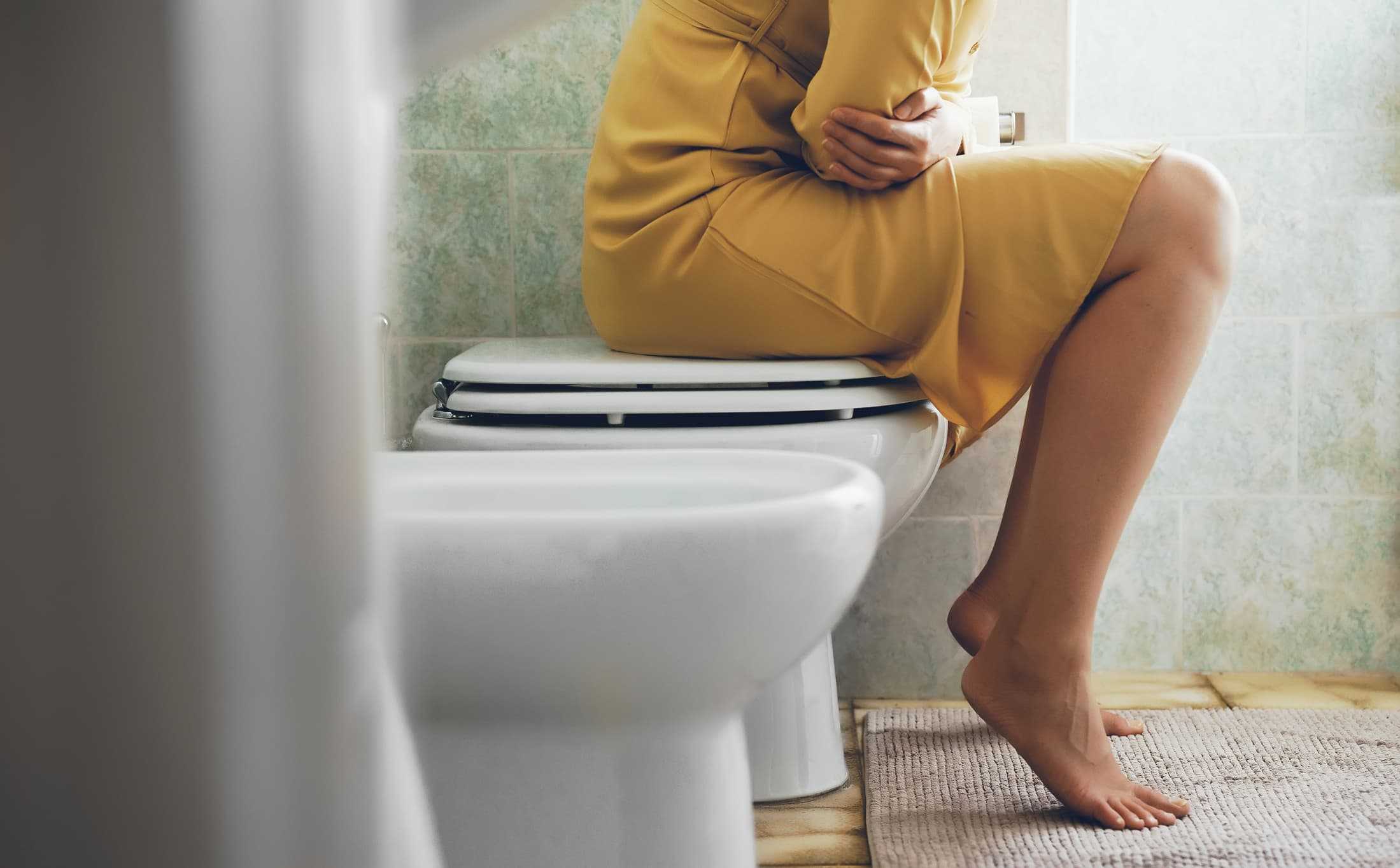 Kvinna med förstoppning sitter på toaletten och håller sig om magen – smärta och svårigheter att tömma tarmen vid förstoppningsbesvär.