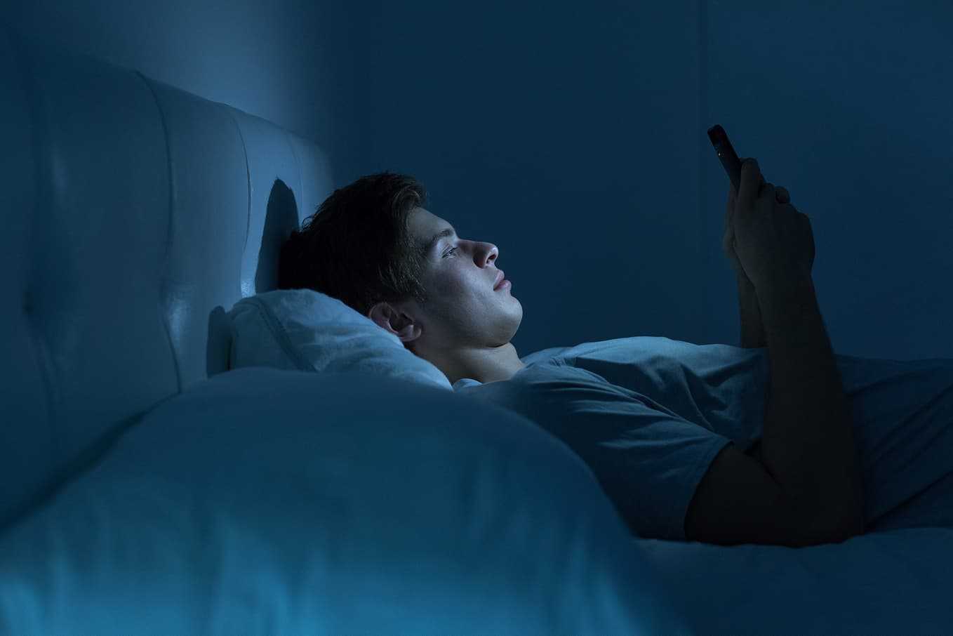 Ung man ligger vaken i sängen på natten och tittar på sin mobiltelefon, bekymrad över för tidig utlösning – information om orsaker, behandling och hjälp hos Doktera.se