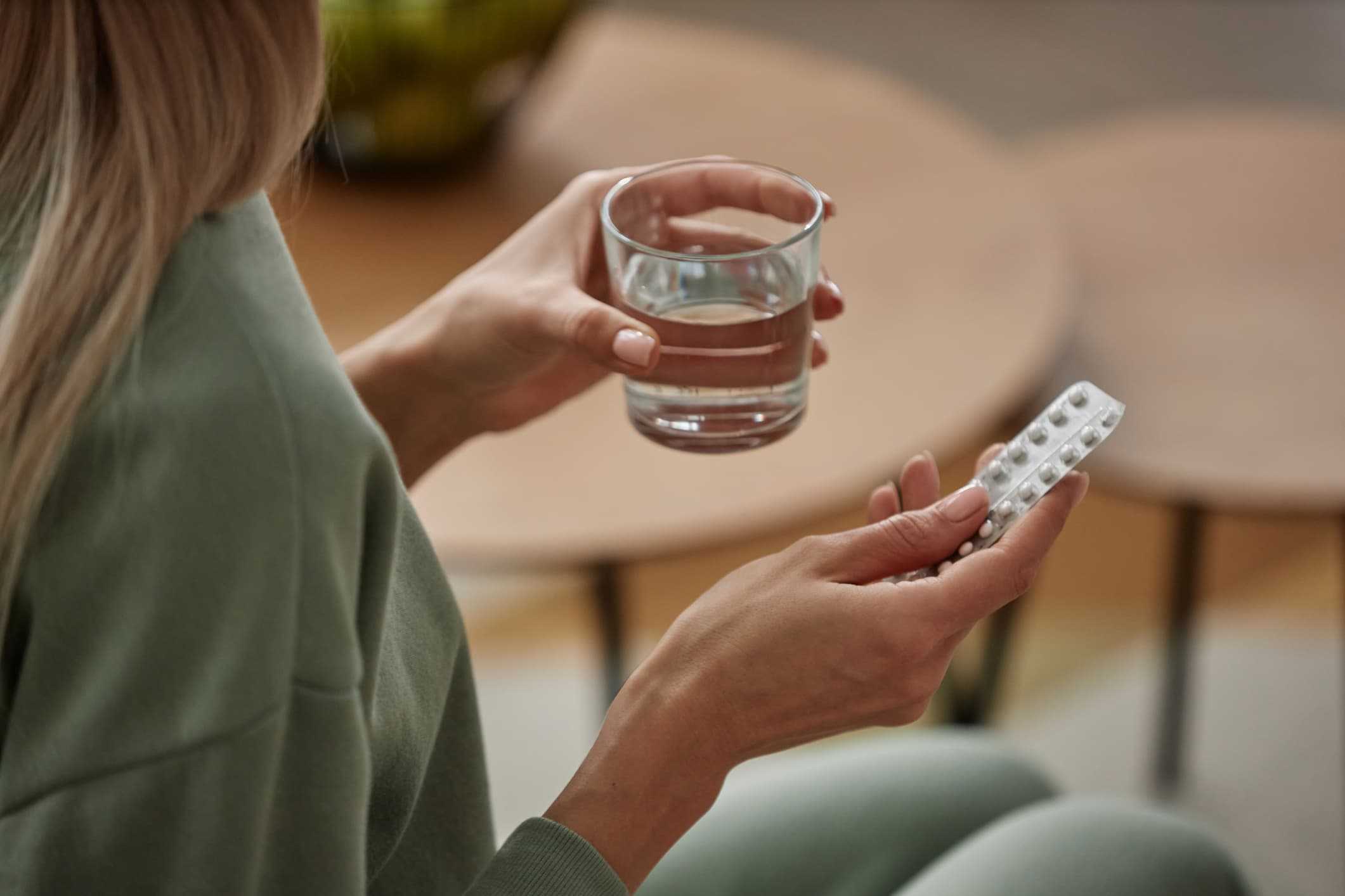 Kvinna håller i glas vatten och tablettkarta – illustrerar användning av läkemedel som Provera eller Primolut Nor för att skjuta upp mensen med hjälp av Doktera.